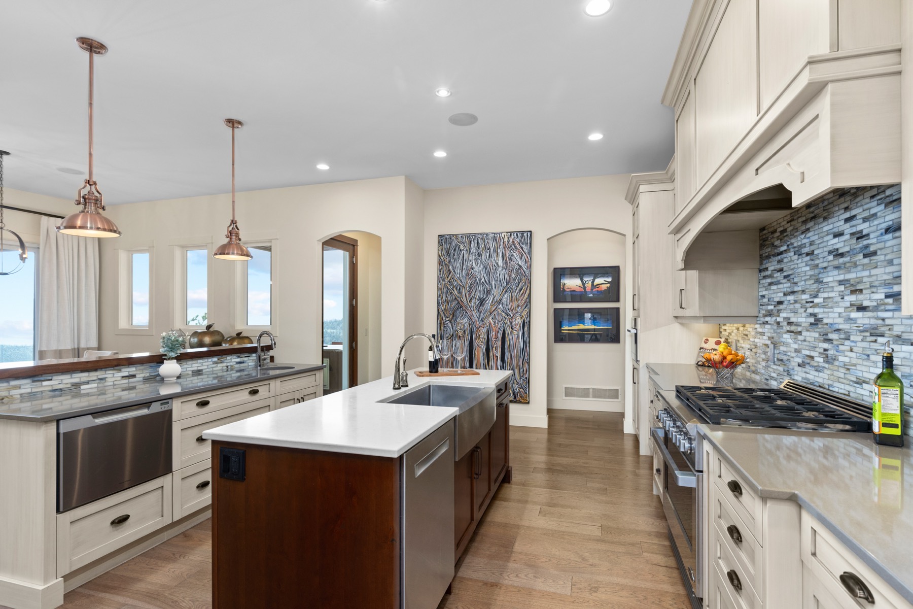 Kitchen with cream cabinetry, a large island with farmhouse sink, professional gas range and a glass tile backsplash.