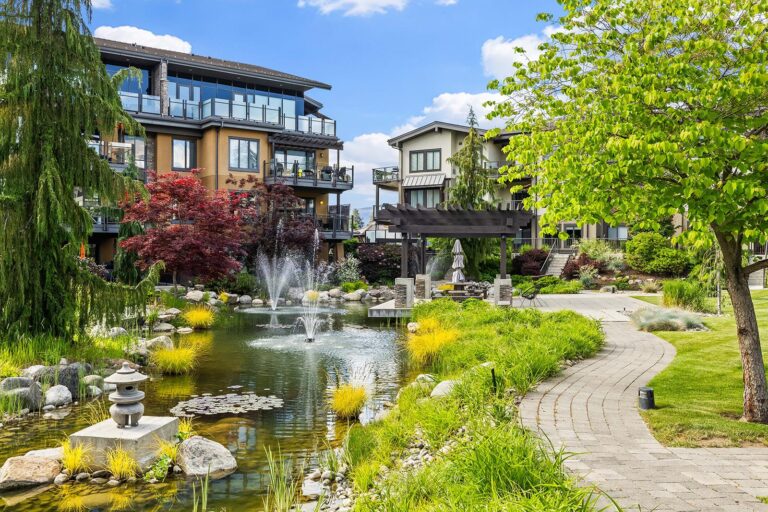 Landscaped pond with fountains, Japanese maples and a paved path, in front of low-rise residential buildings with glass balconies in Lower Mission.