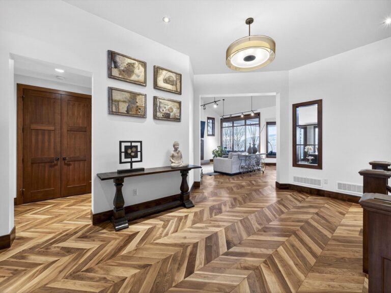 Wide entry hall with herringbone walnut floors, a console table, framed artwork and an open sightline through to a living room.