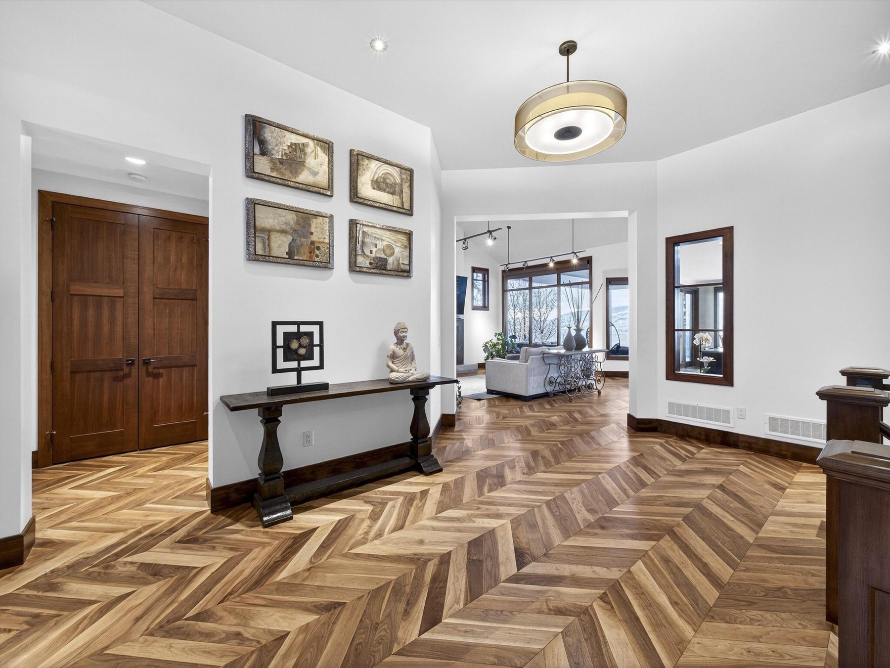 Wide entry hall with herringbone walnut floors, a console table, framed artwork and an open sightline through to a living room.