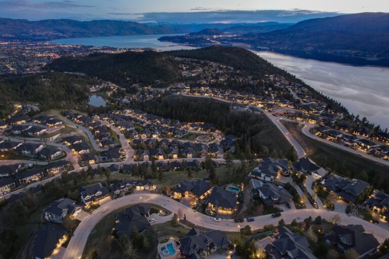 Aerial view of family homes on the Upper Mission hillside at dusk, Okanagan Lake beyond