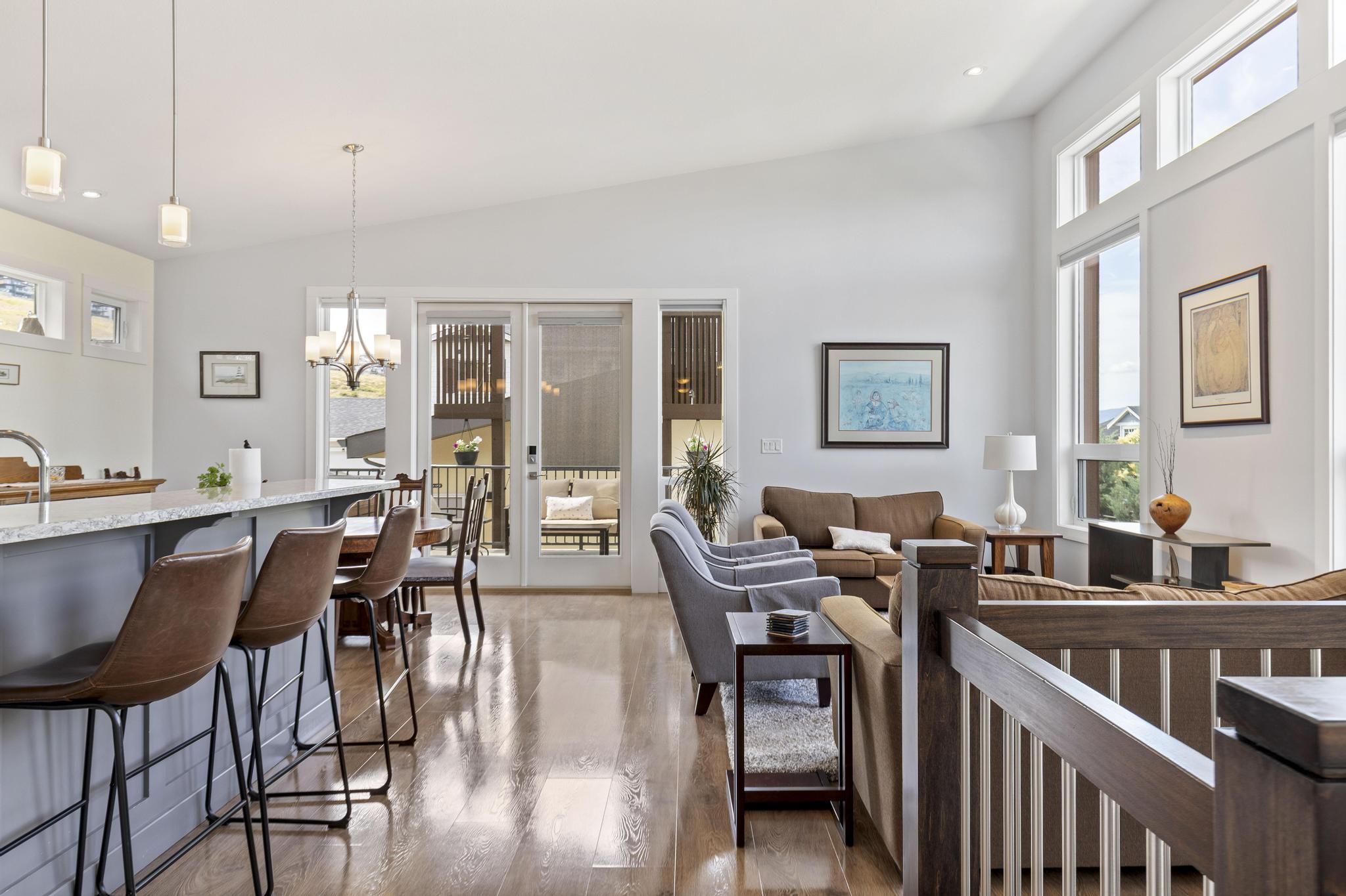 Open-plan kitchen, dining and living area with vaulted ceilings, clerestory windows and french doors to a covered deck in an Upper Mission home in Kelowna