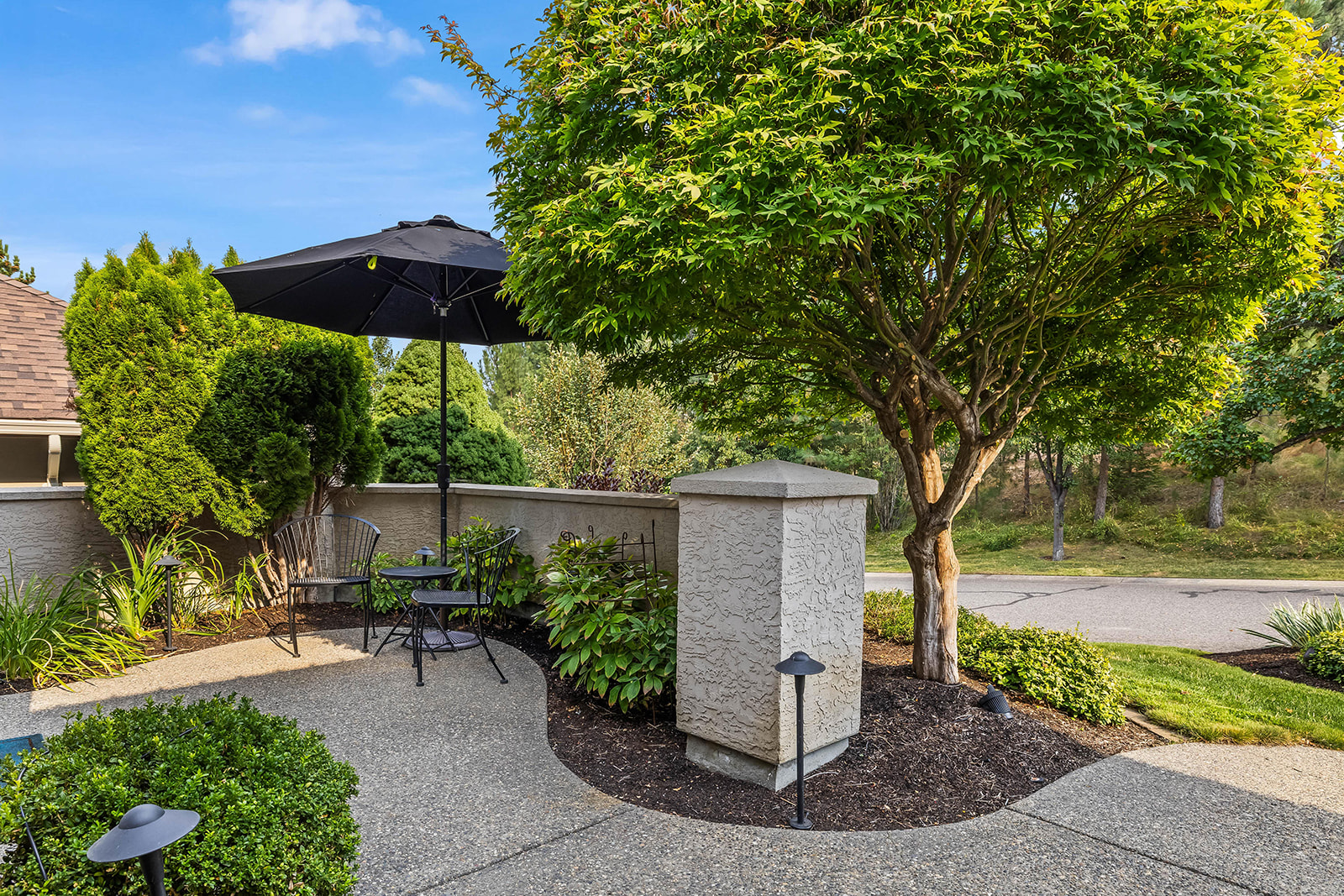 Front courtyard patio with an umbrella table and a maple tree at a Kelowna home